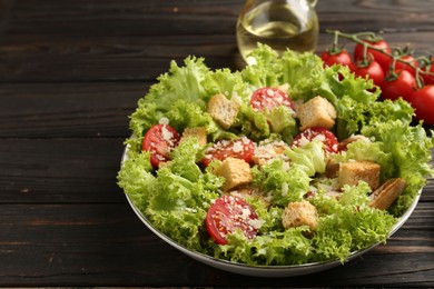Photo of Tasty salad with croutons, tomatoes, cheese and chicken on black wooden table, closeup. Space for text