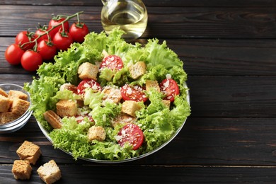 Photo of Tasty salad with croutons, tomatoes, cheese and chicken on black wooden table, closeup. Space for text