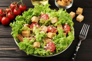 Photo of Tasty salad with croutons, tomatoes, cheese and chicken on black wooden table, closeup