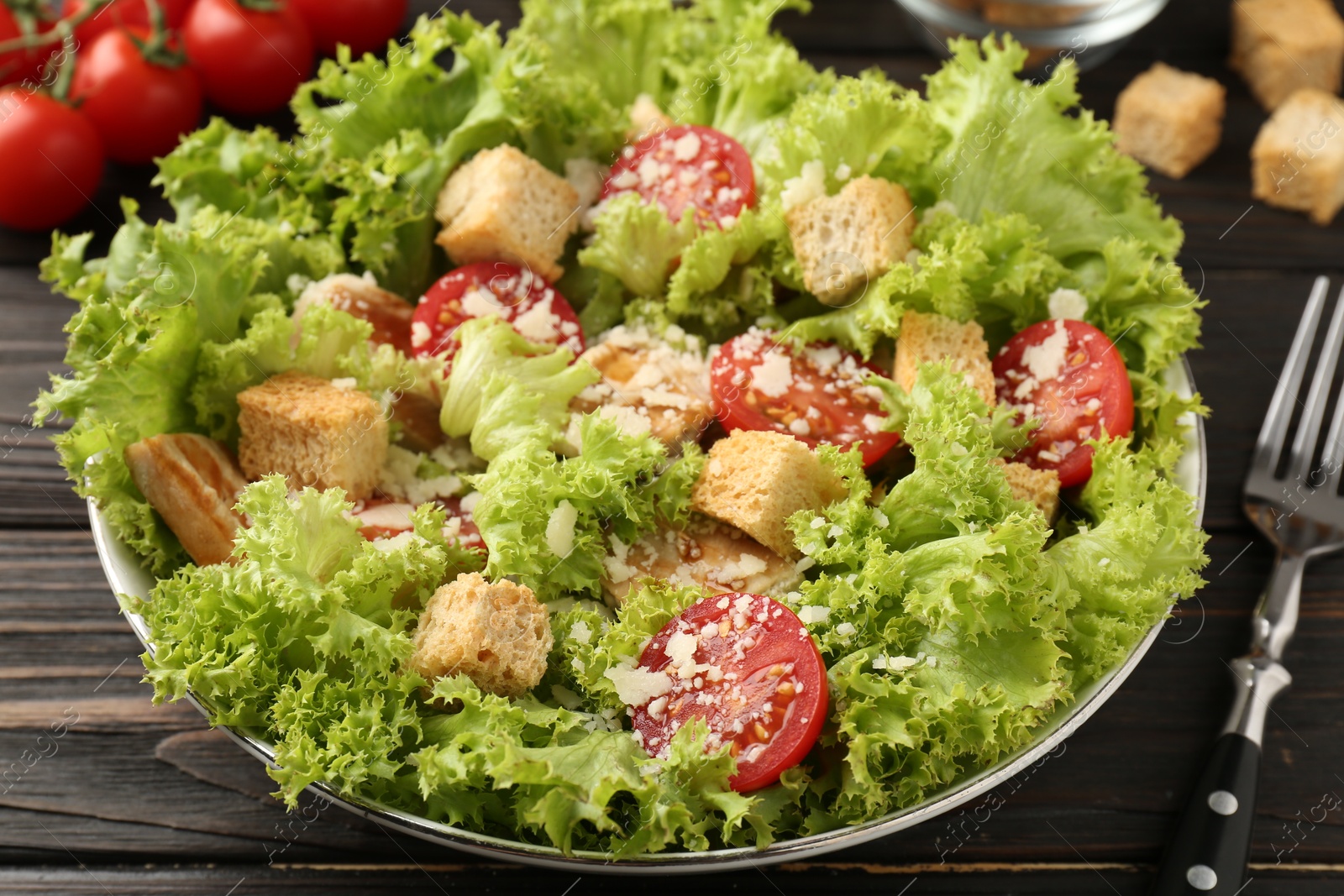Photo of Tasty salad with croutons, tomatoes, cheese and chicken on black wooden table, closeup
