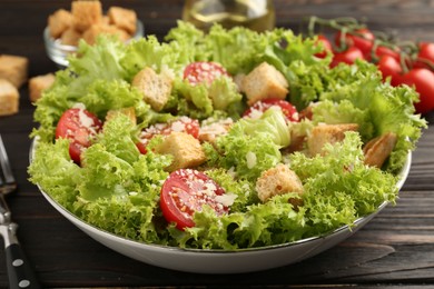Photo of Tasty salad with croutons, tomatoes, cheese and chicken on black wooden table, closeup