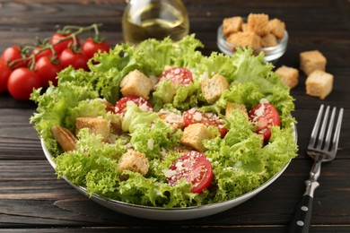 Photo of Tasty salad with croutons, tomatoes, cheese and chicken on black wooden table, closeup