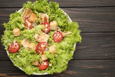 Photo of Tasty salad with croutons, tomatoes, cheese and chicken on black wooden table, top view. Space for text