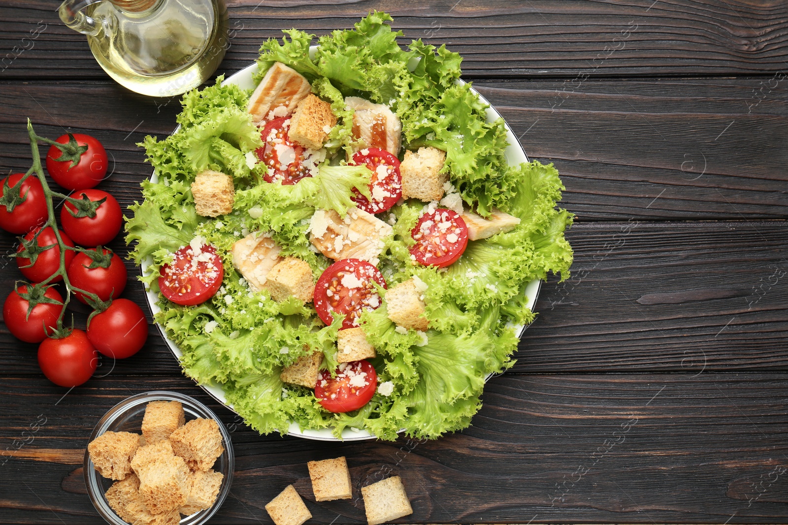 Photo of Tasty salad with croutons, tomatoes, cheese and chicken on black wooden table, flat lay. Space for text