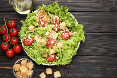 Photo of Tasty salad with croutons, tomatoes, cheese and chicken on black wooden table, flat lay. Space for text
