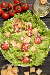 Photo of Tasty salad with croutons, tomatoes, cheese and chicken on black wooden table, flat lay