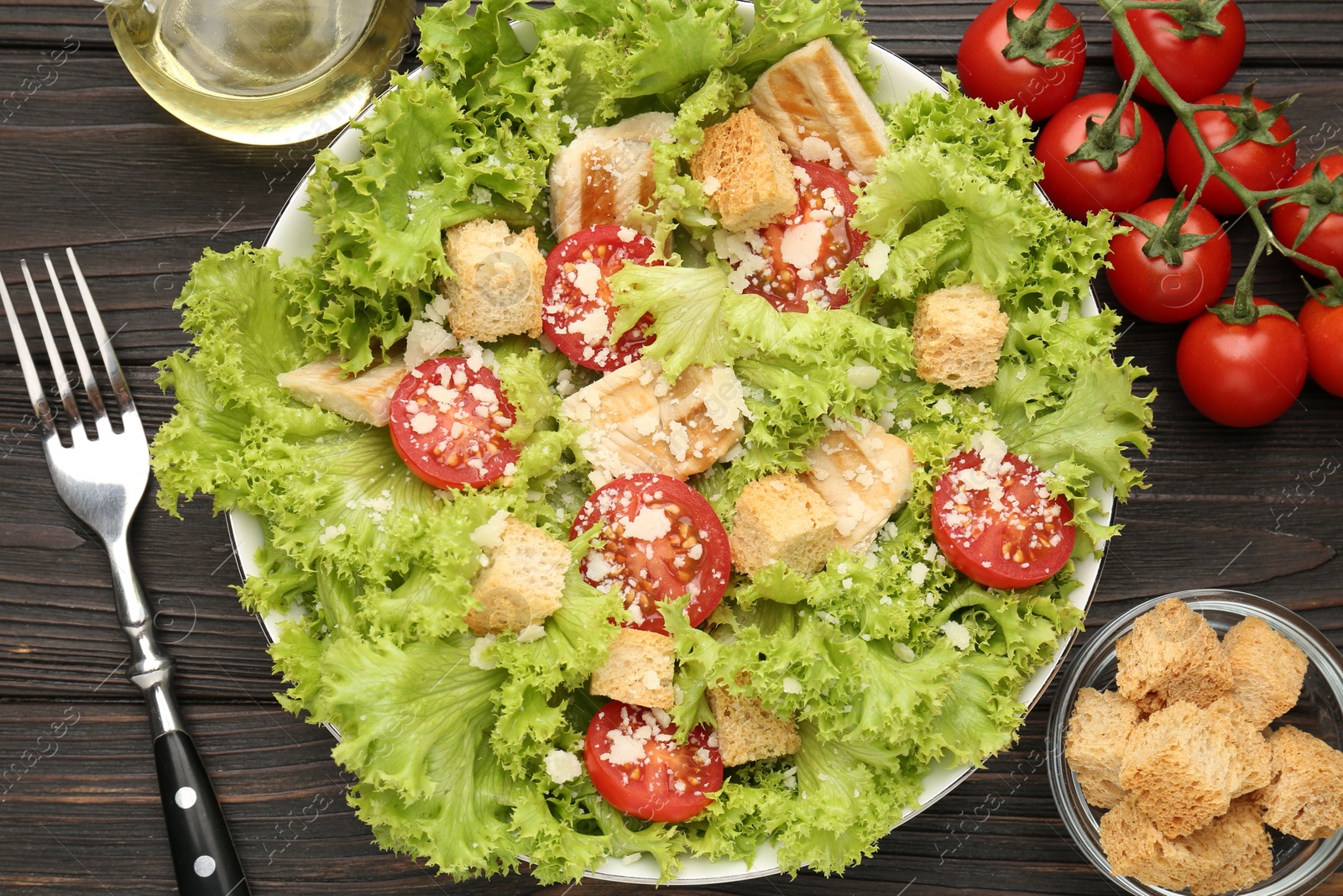 Photo of Tasty salad with croutons, tomatoes, cheese and chicken on black wooden table, flat lay