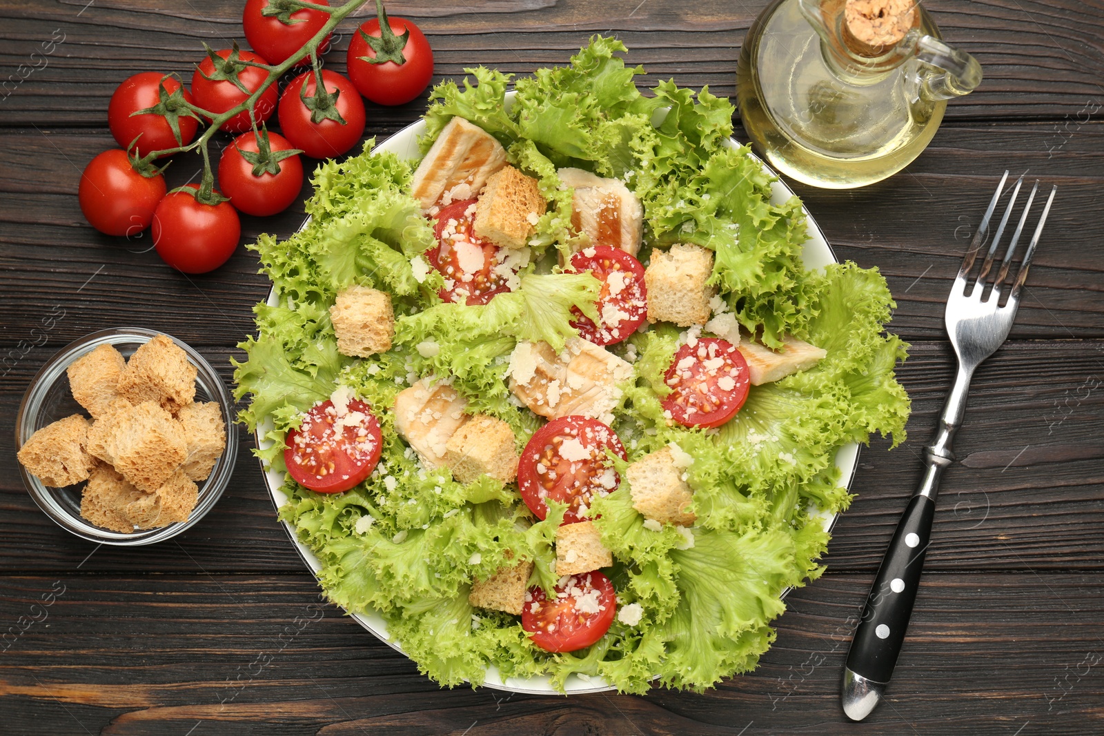 Photo of Tasty salad with croutons, tomatoes, cheese and chicken on black wooden table, flat lay