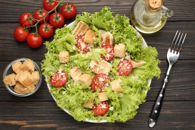 Photo of Tasty salad with croutons, tomatoes, cheese and chicken on black wooden table, flat lay