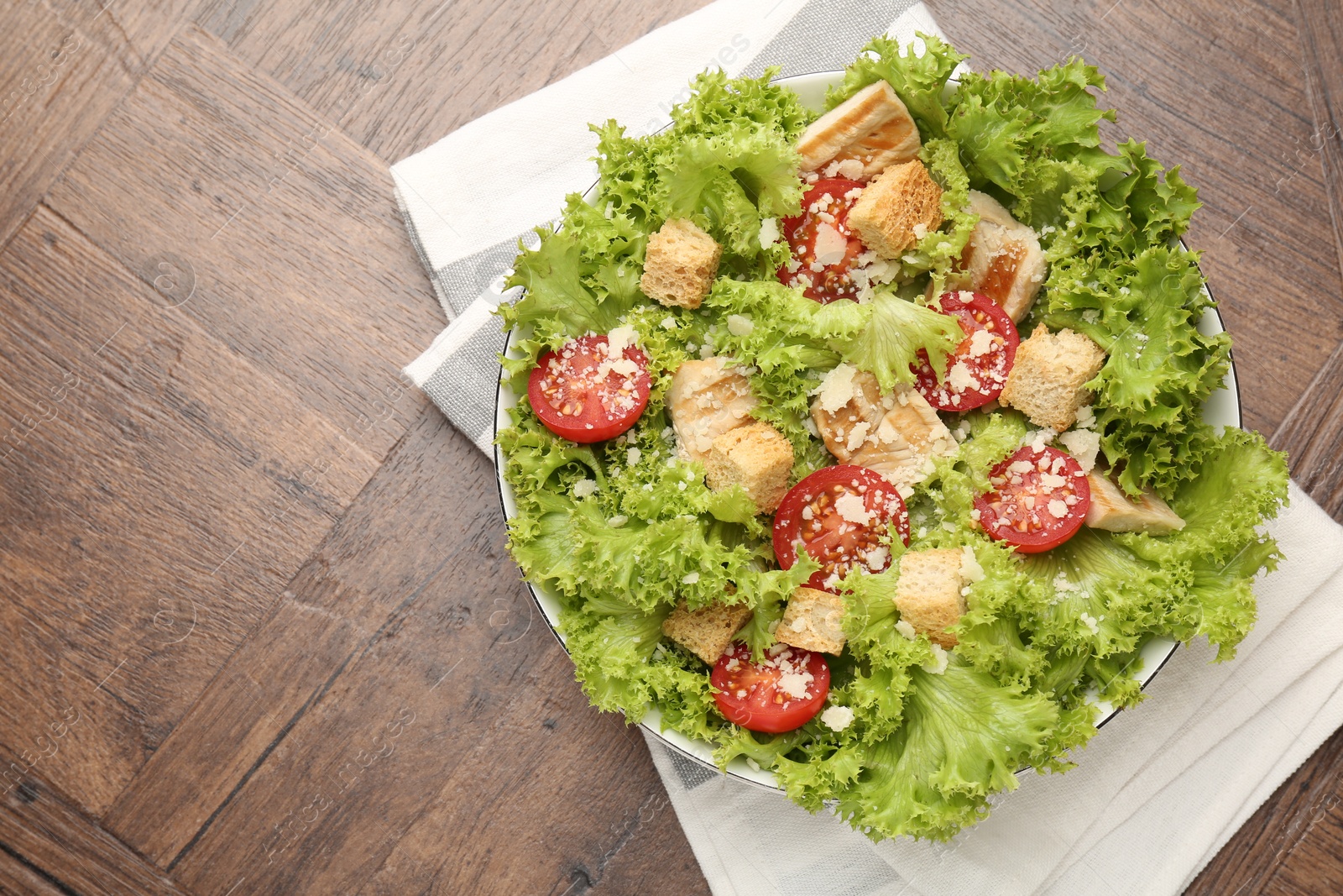 Photo of Tasty salad with croutons, tomatoes, cheese and chicken on wooden table, top view. Space for text