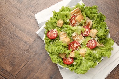 Photo of Tasty salad with croutons, tomatoes, cheese and chicken on wooden table, top view. Space for text