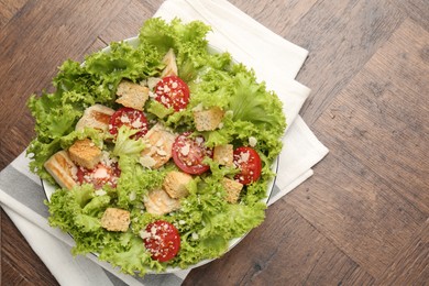 Photo of Tasty salad with croutons, tomatoes, cheese and chicken on wooden table, top view. Space for text