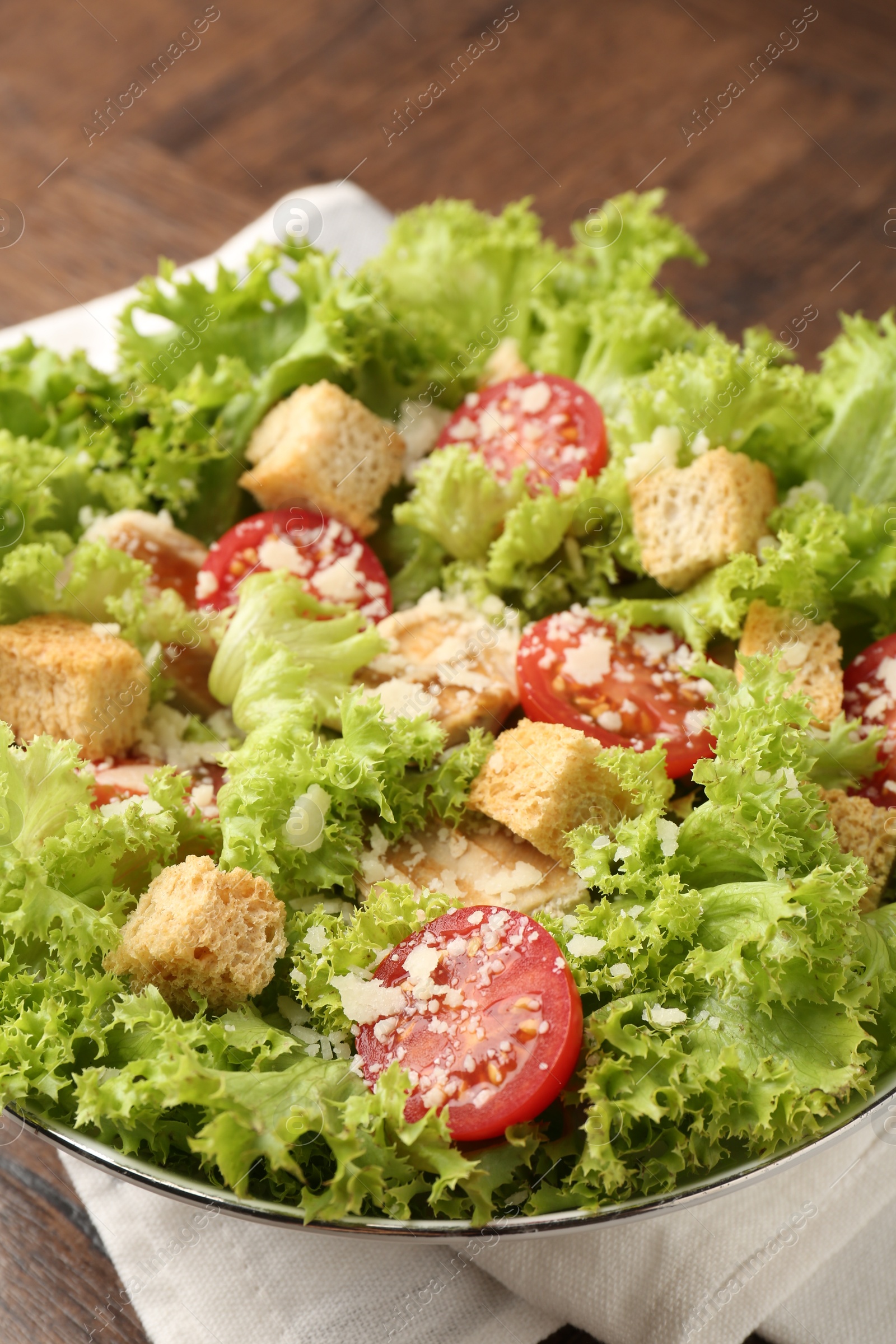 Photo of Tasty salad with croutons, tomatoes, cheese and chicken on wooden table, closeup