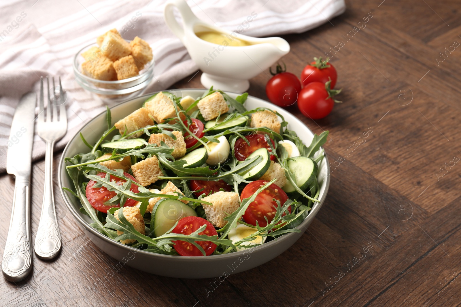 Photo of Tasty salad with croutons, cucumbers, tomatoes and arugula on wooden table, closeup. Space for text