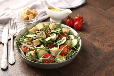 Photo of Tasty salad with croutons, cucumbers, tomatoes and arugula on wooden table, closeup. Space for text