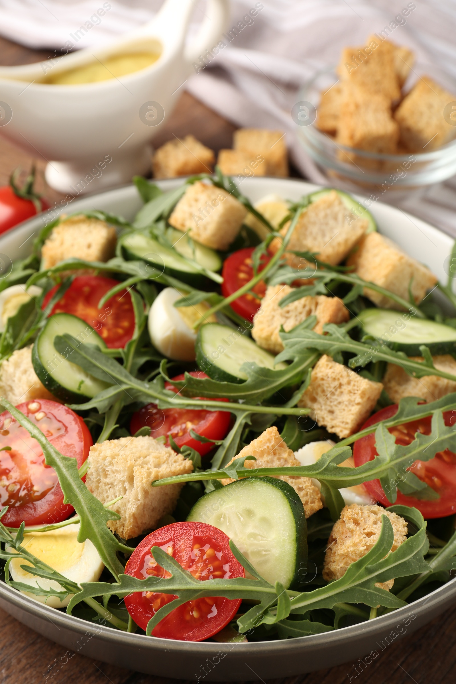 Photo of Tasty salad with croutons, cucumbers, tomatoes and arugula on wooden table, closeup