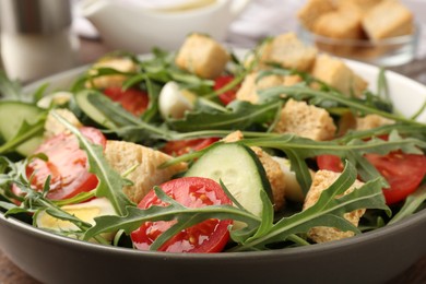 Photo of Tasty salad with croutons, cucumbers, tomatoes and arugula on wooden table, closeup