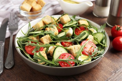 Photo of Tasty salad with croutons, cucumbers, tomatoes and arugula on wooden table, closeup