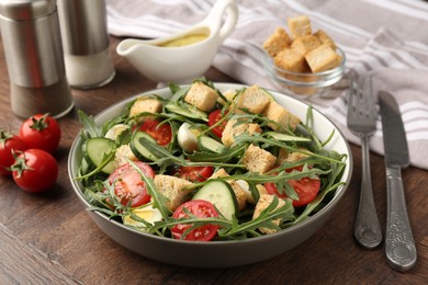 Photo of Tasty salad with croutons, cucumbers, tomatoes and arugula on wooden table, closeup