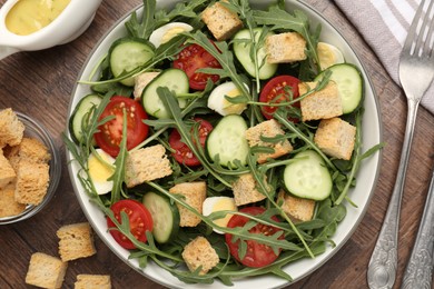 Photo of Tasty salad with croutons, cucumbers, tomatoes and arugula on wooden table, flat lay
