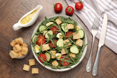 Photo of Tasty salad with croutons, cucumbers, tomatoes and arugula on wooden table, flat lay