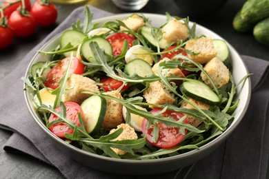 Photo of Tasty salad with croutons, cucumbers, tomatoes and arugula on black table, closeup