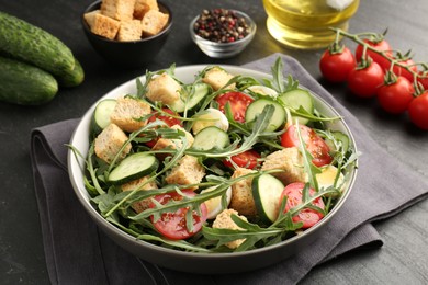Photo of Tasty salad with croutons, cucumbers, tomatoes and arugula on black table, closeup