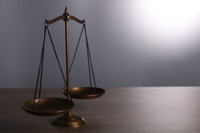 Photo of Scales of justice on wooden table against grey background. Space for text