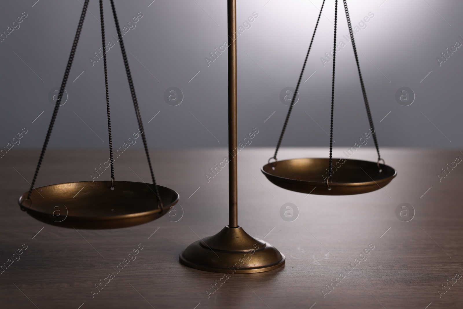 Photo of Scales of justice on wooden table against grey background, closeup