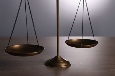 Photo of Scales of justice on wooden table against grey background, closeup