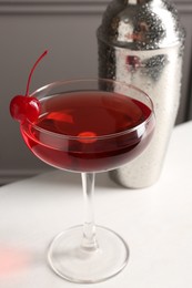 Photo of Tasty cherry cocktail and shaker on white table, closeup