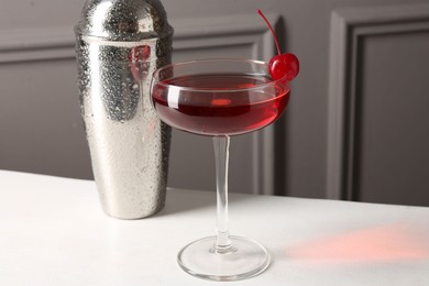 Photo of Tasty cherry cocktail and shaker on white table, closeup