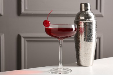 Photo of Tasty cherry cocktail and shaker on white table, closeup