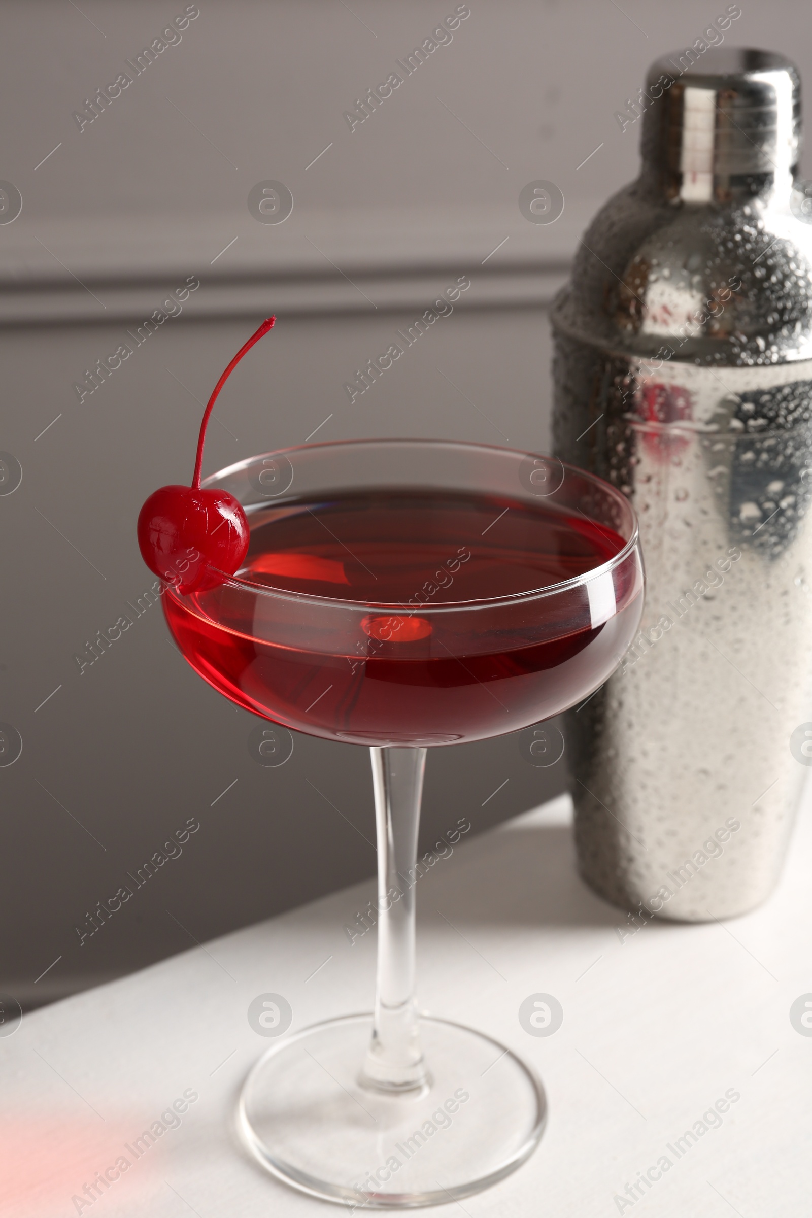 Tasty cherry cocktail and shaker on white table, closeup Photo of Tasty cherry cocktail and shaker on white table, closeup