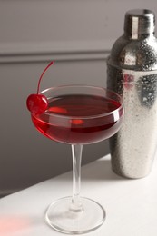 Photo of Tasty cherry cocktail and shaker on white table, closeup