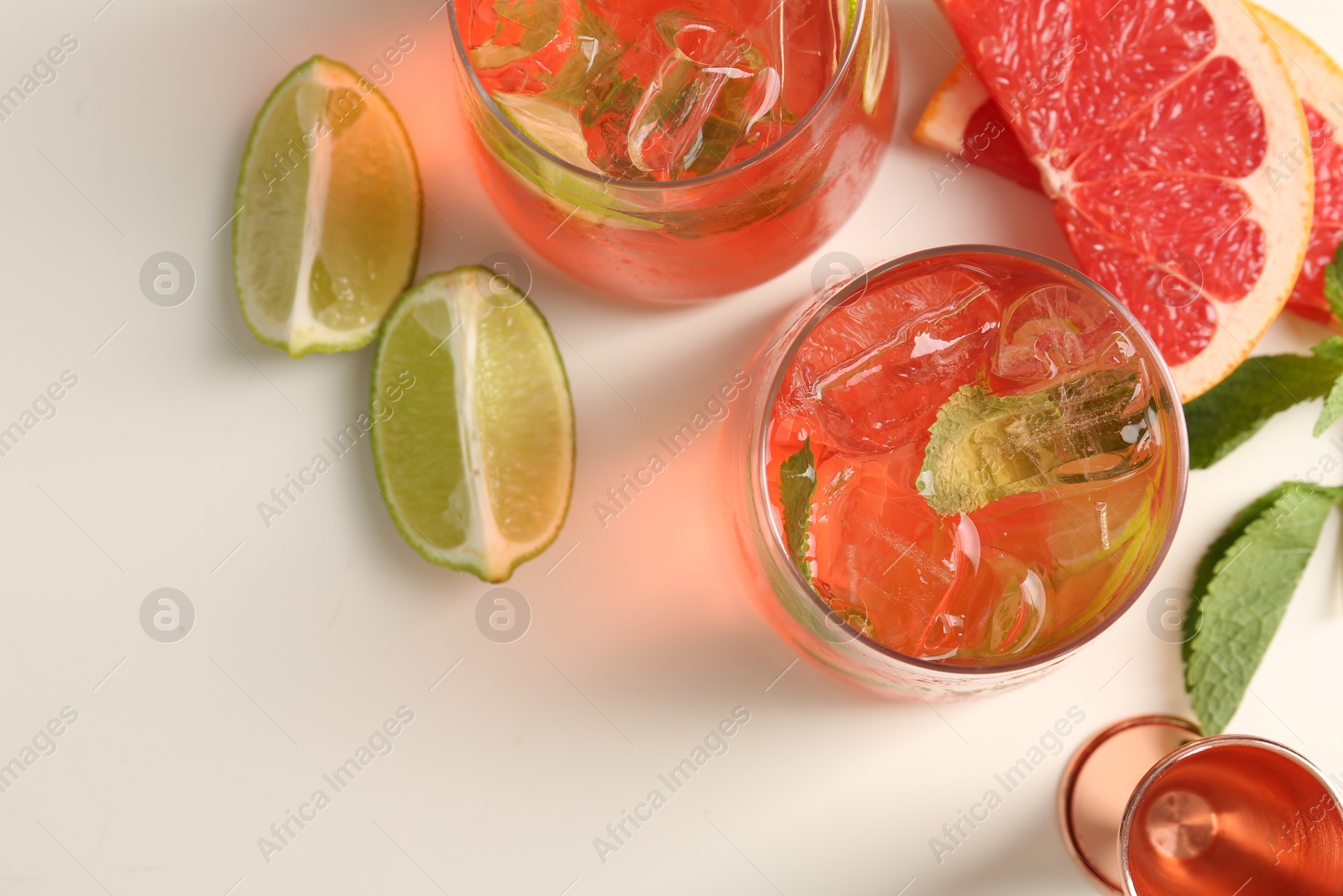Photo of Tasty cocktail with ice cubes, lime and grapefruit on white table, flat lay. Space for text