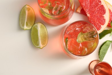 Photo of Tasty cocktail with ice cubes, lime and grapefruit on white table, flat lay. Space for text