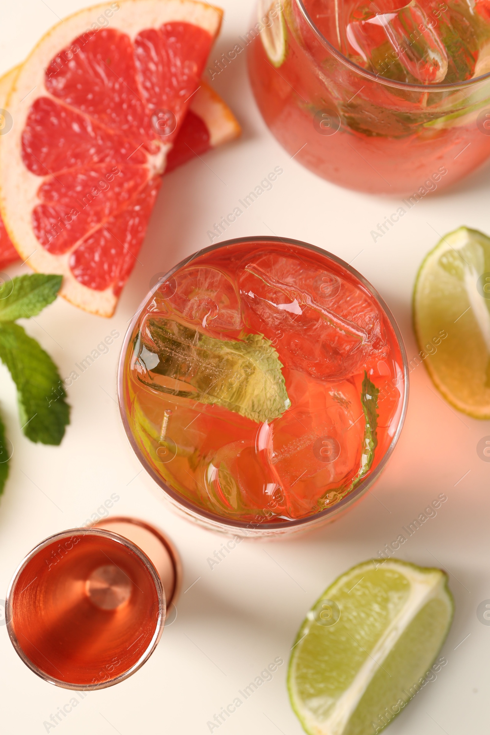 Photo of Tasty cocktail with ice cubes, lime and grapefruit on white table, flat lay