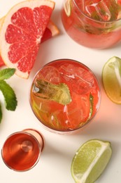Photo of Tasty cocktail with ice cubes, lime and grapefruit on white table, flat lay