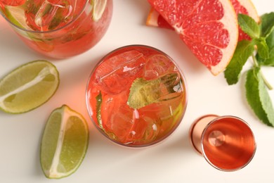 Photo of Tasty cocktail with ice cubes, lime and grapefruit on white table, flat lay