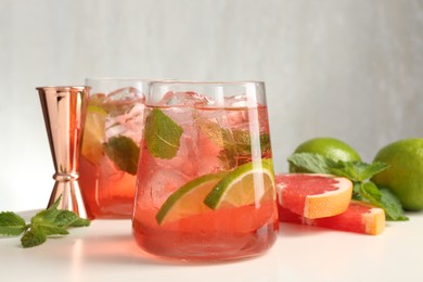 Photo of Tasty cocktail with ice cubes, lime and grapefruit on white table, closeup