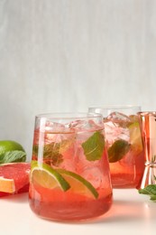 Photo of Tasty cocktail with ice cubes, lime and grapefruit on white table, closeup
