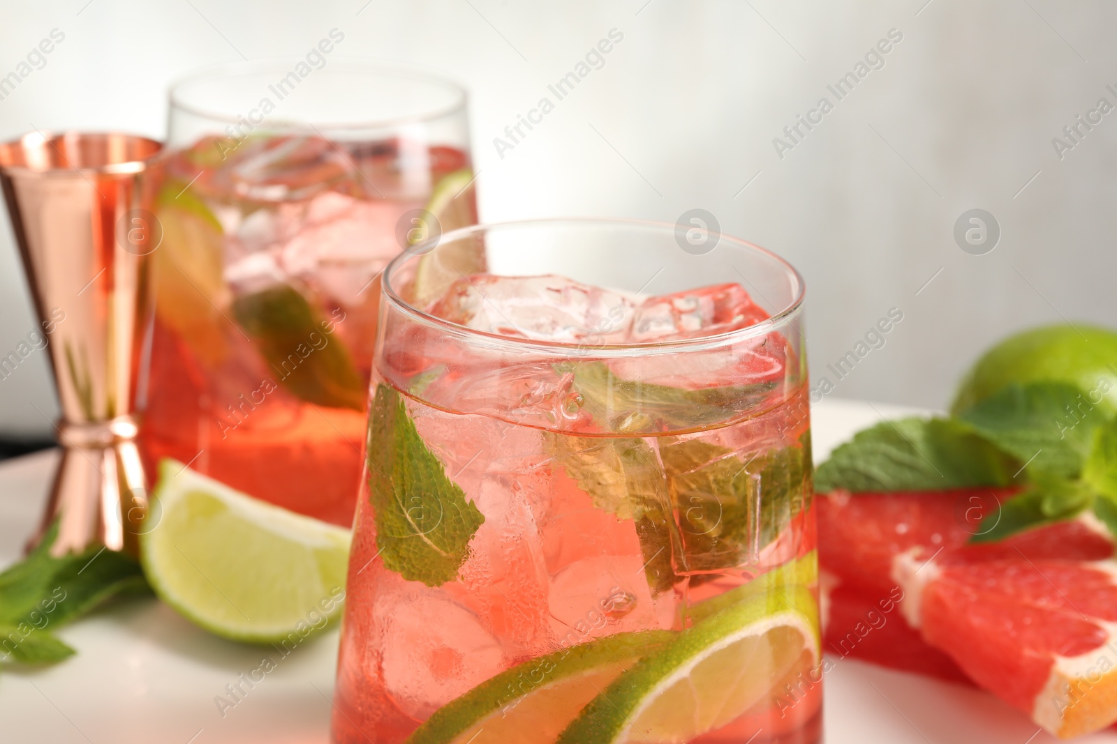 Photo of Tasty cocktail with ice cubes, lime and grapefruit on white table, closeup