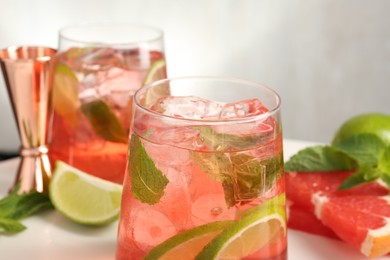 Photo of Tasty cocktail with ice cubes, lime and grapefruit on white table, closeup