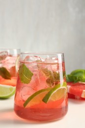 Photo of Tasty cocktail with ice cubes, lime and grapefruit on white table, closeup