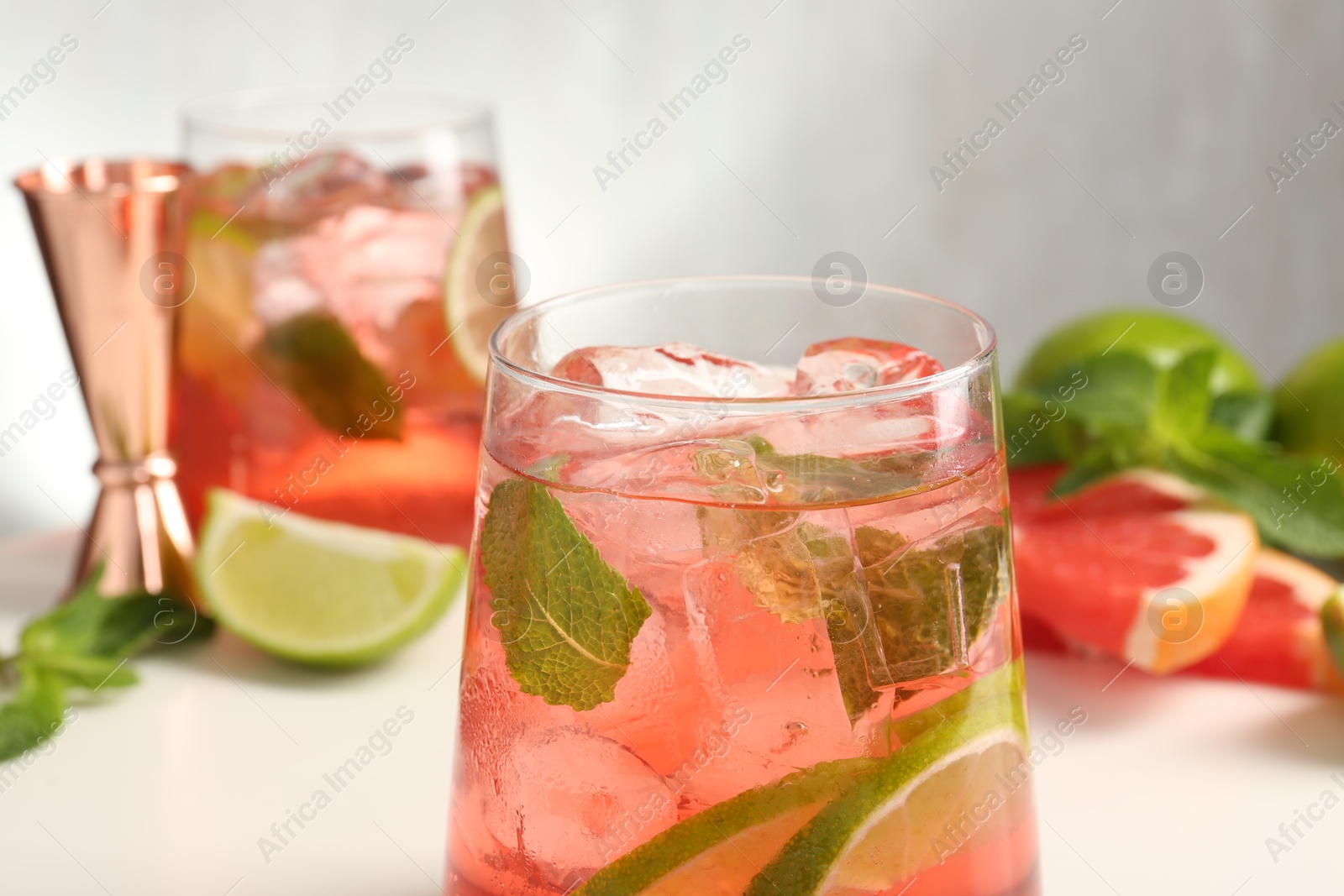 Photo of Tasty cocktail with ice cubes, lime and grapefruit on white table, closeup