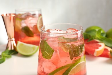 Photo of Tasty cocktail with ice cubes, lime and grapefruit on white table, closeup