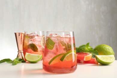 Photo of Tasty cocktail with ice cubes, lime and grapefruit on white table, closeup