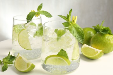 Photo of Tasty cocktail with lime and ice cubes on white table, closeup