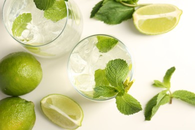 Photo of Tasty cocktail with lime and ice cubes on white table, flat lay